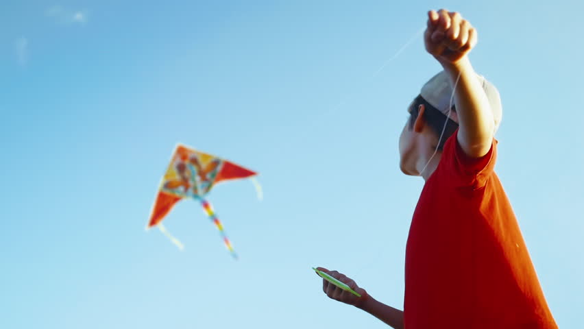 Boy Launches a Colored Kite Into the Blue Sky. The Little Kid Controls a Kite On a Sunny Day. The Concept of Freedom, Children's Happiness. Carefree Happy Childhood. Slow Motion. Sun Flares | Shutterstock HD Video #1100579125