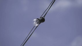Handheld closeup video of a light bulb fixed on a wire outdoors.