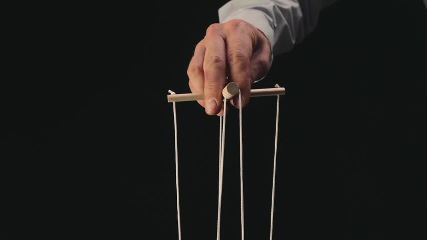 The puppeteer's hand controls the puppet with a wooden manipulator and strings. The marionettist controls and pulls the strings on a black isolated background. Close up. Royalty-Free Stock Footage #1100582361