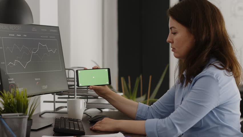 Female manager looking at horizontal greenscreen on mobile phone, working in corporate office with chroma key display. Young woman analyzing smartphone screen with isolated mockup. | Shutterstock HD Video #1100583347