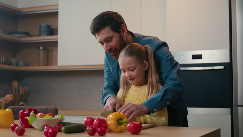 Father teaching Caucasian kid daughter cut fresh vegetable salad in kitchen cooking happy family together. Parent dad learning small child girl cook healthy food help with cutting cucumber for meal Royalty-Free Stock Footage #1100584715