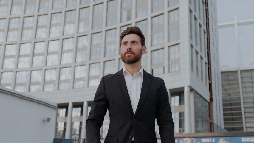 A successful confident businessman in a business suit walks against the backdrop of a business center. | Shutterstock HD Video #1100594021
