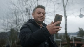 Short-haired, Fair-skinned Young Man Having a Video Chat on his Smartphone Outdoors