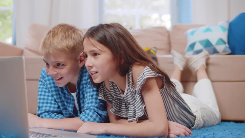 Children brother and sister use laptop at home. Kids siblings play on computer. Preteen boy and girl use laptop computer lying on floor in living room. Childhood, technology concept. Realtime.  | Shutterstock HD Video #1100603207