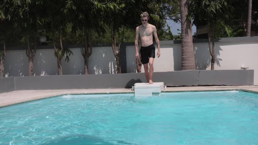 Funny man jumping in swimming pool excited for summer having fun splashing in water enjoying summertime swim on vacation. slow motion