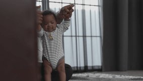A heartwarming video of a african american father teaching his toddler to walk, providing support and encouragement with every step, in the comfort of their home. father's day and family