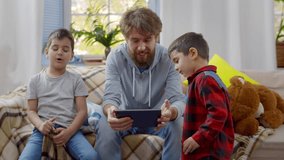 Happy father using tablet computer with children. Dad with kids play game on touchscreen technology. Little boys with father play on digital tablet. Happy family, fatherhood concept. Realtime