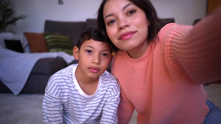 Point of view of young mother and son on a video call with their family being connected in the distance. Latin American single mom and child looking at camera waving happily. Royalty-Free Stock Footage #1100612907