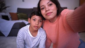 Point of view of young mother and son on a video call with their family being connected in the distance. Latin American single mom and child looking at camera waving happily.