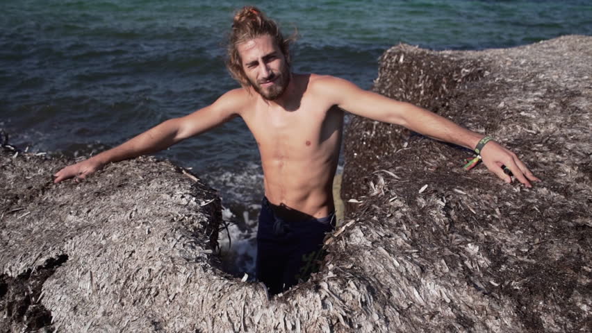 Boy with ponytail and beard among a mountain full of seaweed