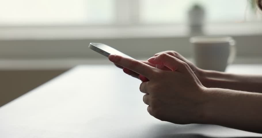 Hands of unknown female using modern smart phone seated at desk indoors, close up view. Sharing sms, messaging through messenger, mobile application usage for communication, spend leisure on internet Royalty-Free Stock Footage #1100614237