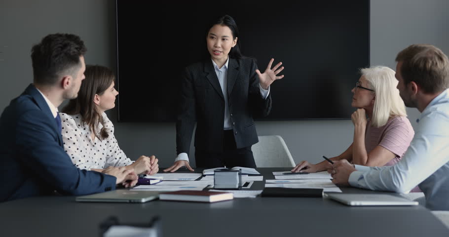 Asian business coach makes presentation, share information to team, looks confident leads formal meeting with company investors or clients sit at desk gathered in boardroom. Corporate training event Royalty-Free Stock Footage #1100614263