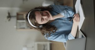 Young woman in headphones studying use video call, make notes, jotting information, receive new knowledge through online e-learning with help of on-line tutor. Virtual meeting event to gain new skills