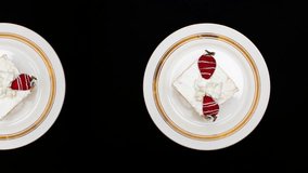 4K looped food video. Top view. Square cake with whipped cream, fresh sweet strawberries. Round white plate with golden border with delicious piece of cake on black dark background moves endlessly