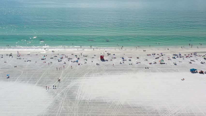 People chilling on white sand of wide Siesta Key Beach, beach is groomed and ocean water is turquoise; top down view