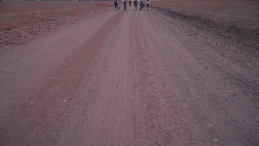 Establisher wide view of group of trekkers with backpacks in middle of vast rural road, mountain range background landscape