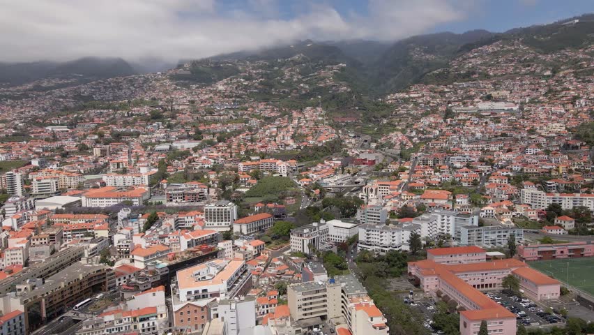 Aerial view the city of Funchal, capital of Madeira, Portugal. View of entire city and the mountains with beautiful clouds in the background. Drone flying right