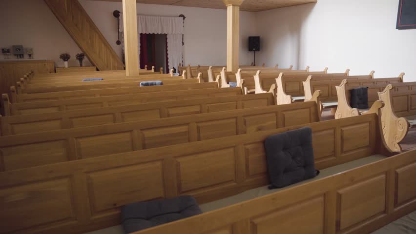 Rows of pews inside small, empty reformed church. Tracking, view from front. Royalty-Free Stock Footage #1100620931