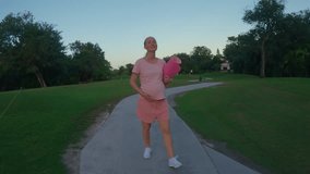A stunning slow-motion stock video captures a beautiful moment of motherhood. A pregnant woman, dressed in a pink t-shirt and shorts, walks gracefully through a lush green field with a yoga mat in
