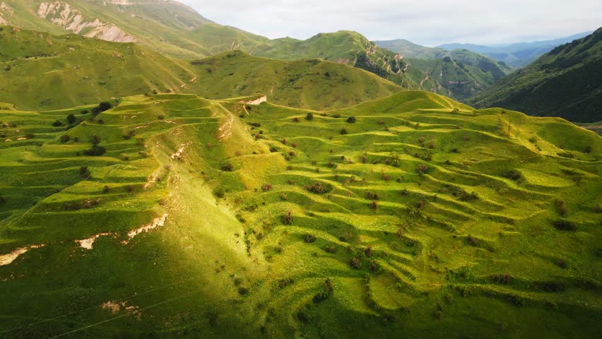 View of the green agricultural terraces and mountains at sunset.  Aerial drone view. Chokh village in Dagestan, Russia. Beautiful summer landscape.

