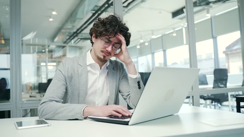 Portrait of sad business man freelancer suffering headache painful feelings chronic migraine pressure working on computer at modern glass office Stressed entrepreneur feels hurt at workplace indoors | Shutterstock HD Video #1100626105