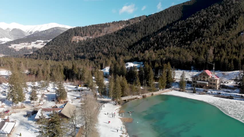 Dobbiaco Lake with forest and snow, aerial view in winter