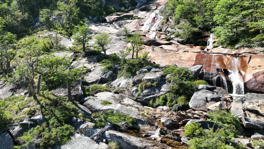 Aerial drone nature footage of green  forest and transparent waterfalls around Nahuel Huapi Lake, Patagonia, Bariloche, Argentina. It captures the beautiful sunny tranquility