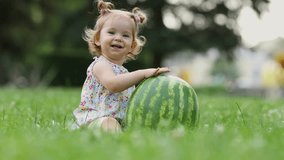little girl with a funny hairstyle eats a watermelon on the lawn in the park. healthy snack for kids. child eats fruit outdoors.high quality 4K video