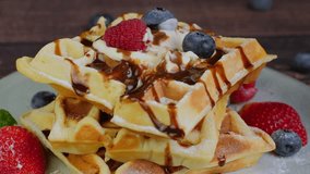 Person eating soft Belgian waffles using a fork, cutting a piece of sweet fluffy waffle with cream topping and chocolate syrup, served with fresh berries, close up video, high quality 4k footage