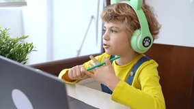 Cute smart caucasian primary School Child with headphones educate online laptop. Tutor teaching digital class, web lesson on computer at home. Virtual education course. Schoolboy girl studying doing