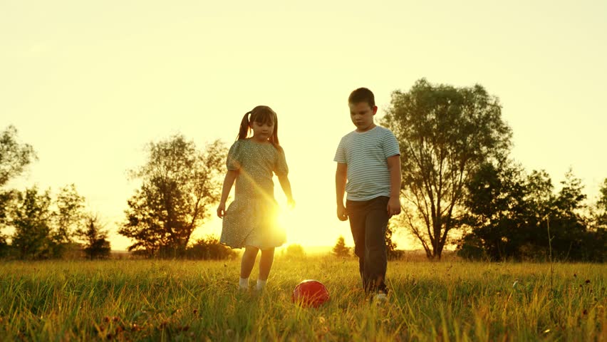 Happy child runs, kicks ball, Boy girl playing football in summer meadow. Happy family, nature. Children playing football outdoors. Active child, boy, girl playing with red ball in park on green grass Royalty-Free Stock Footage #1100632613