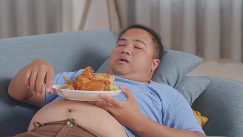 Close Up Of A Fat Asian Man Eating Fast Food Having Fried Chicken While Lying On A Sofa In The Living Room At Home
 Royalty-Free Stock Footage #1100636861