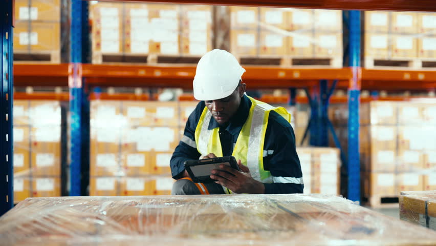 Warehouse workers holding digital tablet checking inventory management packaging boxes. Black african man counting box goods on shelves at storehouse | Shutterstock HD Video #1100638663
