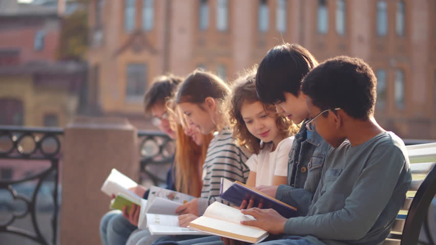 Teen students read book outdoors on bench. Multiethnic school kids read and do homework outside. Diverse children sit on bench and read book. Childhood, education concept. Realtime  Royalty-Free Stock Footage #1100638775
