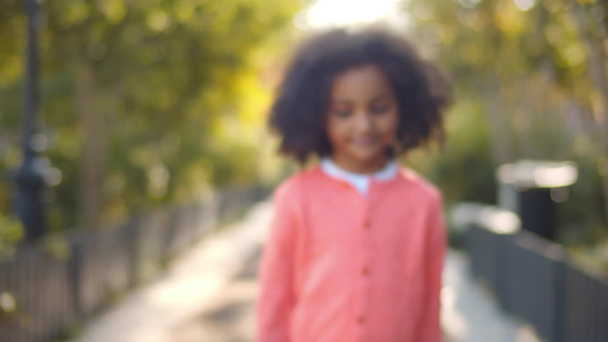 Funny African-American little girl smiling looking at camera outdoors. Cute kid smile at camera. Adorable preschool girl posing at camera outside. African-American child portrait. Realtime
