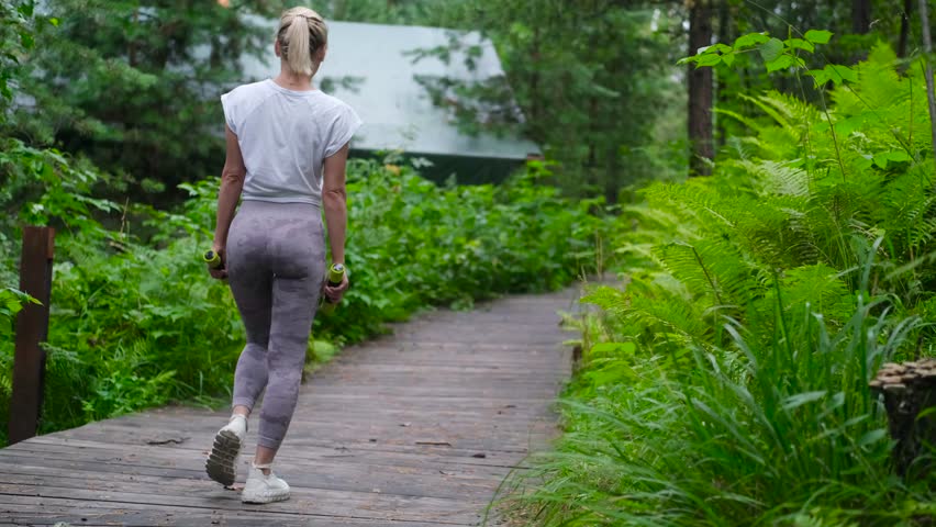 Beautiful sportswoman doing squats, lunges with dumbbells in the forest, during summer outdoor recreation