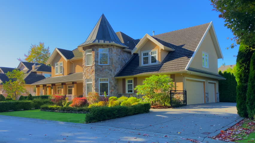 Establishing shot of two story stucco luxury house with garage door, big tree and nice Fall Foliage landscape in Vancouver, Canada, North America. Day time on Sept 2021. ProRes 422 HQ.