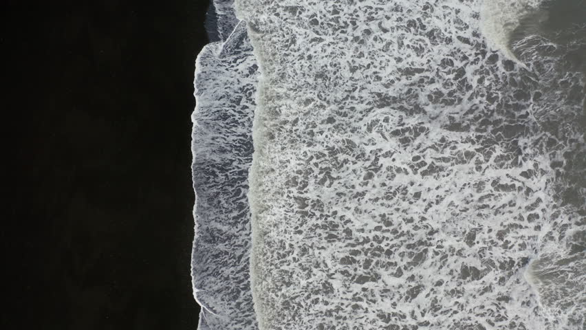Aerial: Top down aerial view of waves breaking on volcanic black sand beach