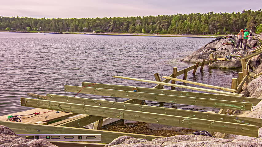 Men workers building wooden frame on rocky lake coastline, fusion time lapse