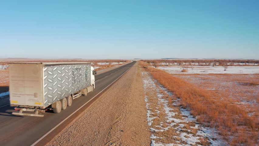 Rear view of a truck driving on a desert road outside the city with a snow-covered roadside
