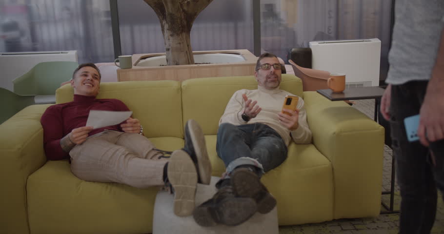 Male colleagues joined by another colleague while resting on the cozy office sofa, modern and exclusive office space | Shutterstock HD Video #1100651907