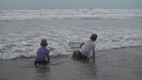 Little boys are playing with waves on the beach, Bali, Indonesia. High quality 4k footage