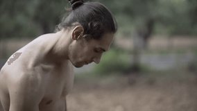 Shirtless athletic spanish man straps a backpack in the forest and goes away.