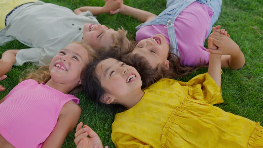Happy friends lying in the grass, holding each other hands and having fun. Top view. | Shutterstock HD Video #1100654439