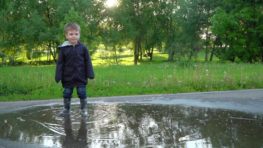 Boy in rubber boots jumping in a puddle in park Royalty-Free Stock Footage #1100655593