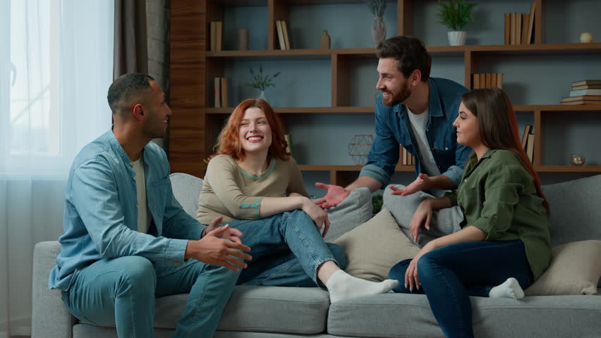 Four ethnic friends fellows companions sit on home couch talking discuss plans chatting friendly talk indoors gathered multiethnic men and women converse joking laughing sharing news real friendship | Shutterstock HD Video #1100655731