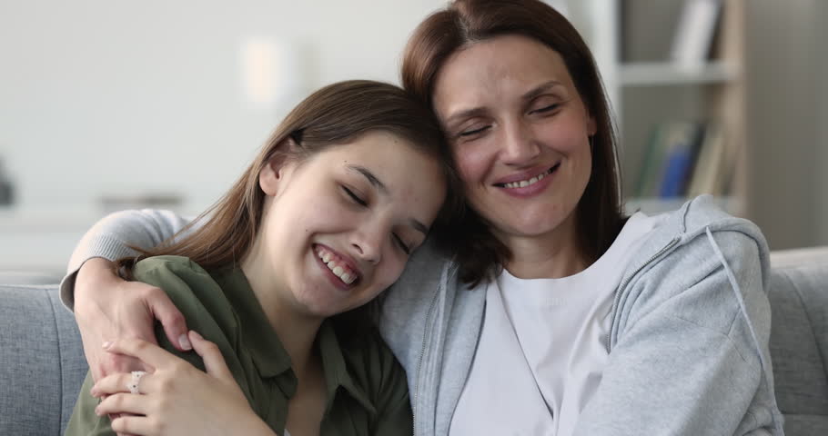 Close up loving mature woman enjoy tender moment, kiss, hugs her teenager daughter sit together on sofa. Happy motherhood, understanding and harmonic good friendly relations between teen child and mom Royalty-Free Stock Footage #1100656535