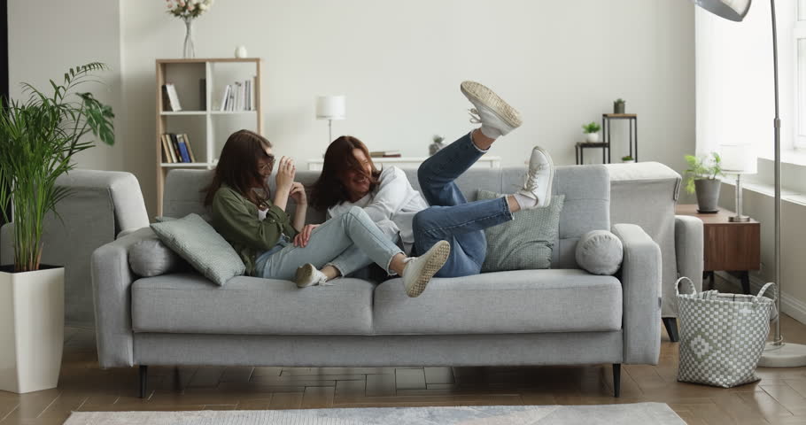 Happy family, mom and daughter jump on soft sofa, laugh, enjoy vacation, relaxing, celebrate move to new own home, spend carefree peaceful weekend, relish vacation, looking playful and crazy together | Shutterstock HD Video #1100656559