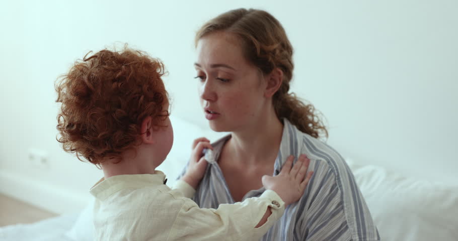 Young pretty mother comforting crying, disobedient tired toddler son before daytime healthy nap, embracing and talk to him, calming, express care and love, close up. Motherhood, upbringing, childhood Royalty-Free Stock Footage #1100656589