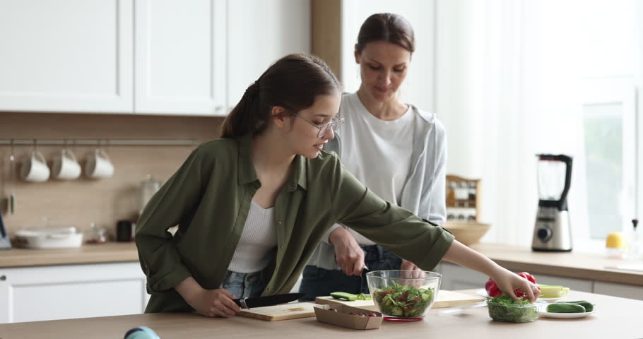 Middle-aged mother cooking with pretty teen daughter, prepare vegetarian salad together, talking standing in cozy kitchen, spend leisure, lead warm conversation enjoy cookery at home. Family weekend Royalty-Free Stock Footage #1100656621